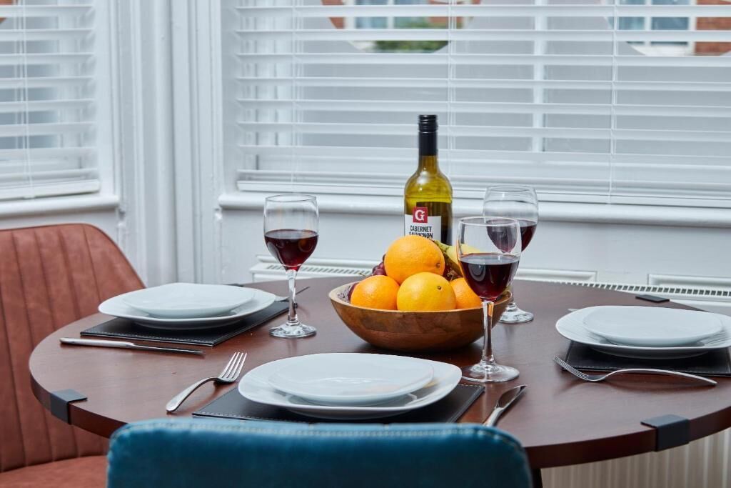 A dining table set with plates, glasses, a bottle, and a bowl of fruit.