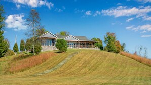 A two-story house with a stone foundation, large windows, and a covered porch. - Calaboose Retreat- Hot Tub, Outdoor Pool, Pool Table, FirePit, Fireplace (Campton)