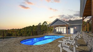 A swimming pool with a stone deck, surrounded by a wooden fence and a covered patio area with seating. - Calaboose Retreat- Hot Tub, Outdoor Pool, Pool Table, FirePit, Fireplace (Campton)