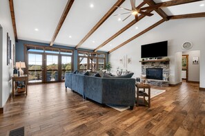 A spacious living room with a large sofa, a fireplace, and a television. - Calaboose Retreat | Seasonal Outdoor Pool, Hot Tub, Pool Table, Firepit, Fireplaces (Campton)