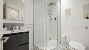 Uma casa de banho moderna com cabine de duche em vidro, sanita e lavatório com espelho em cima.