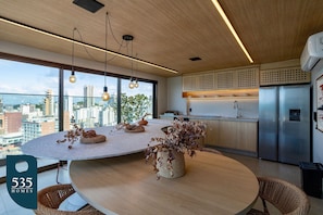 A modern kitchen with a large island, stainless steel appliances, and a city view through large windows. - Studio with sea view steps from Barra Beach (Salvador)