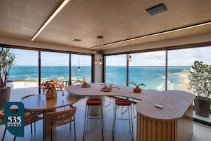 A modern kitchen with a large island, large windows, and a view of the ocean. - Studio with sea view steps from Barra Beach (Salvador)