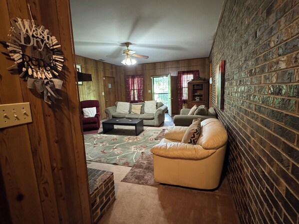A cozy living room with a fireplace, a ceiling fan, and a brick wall.