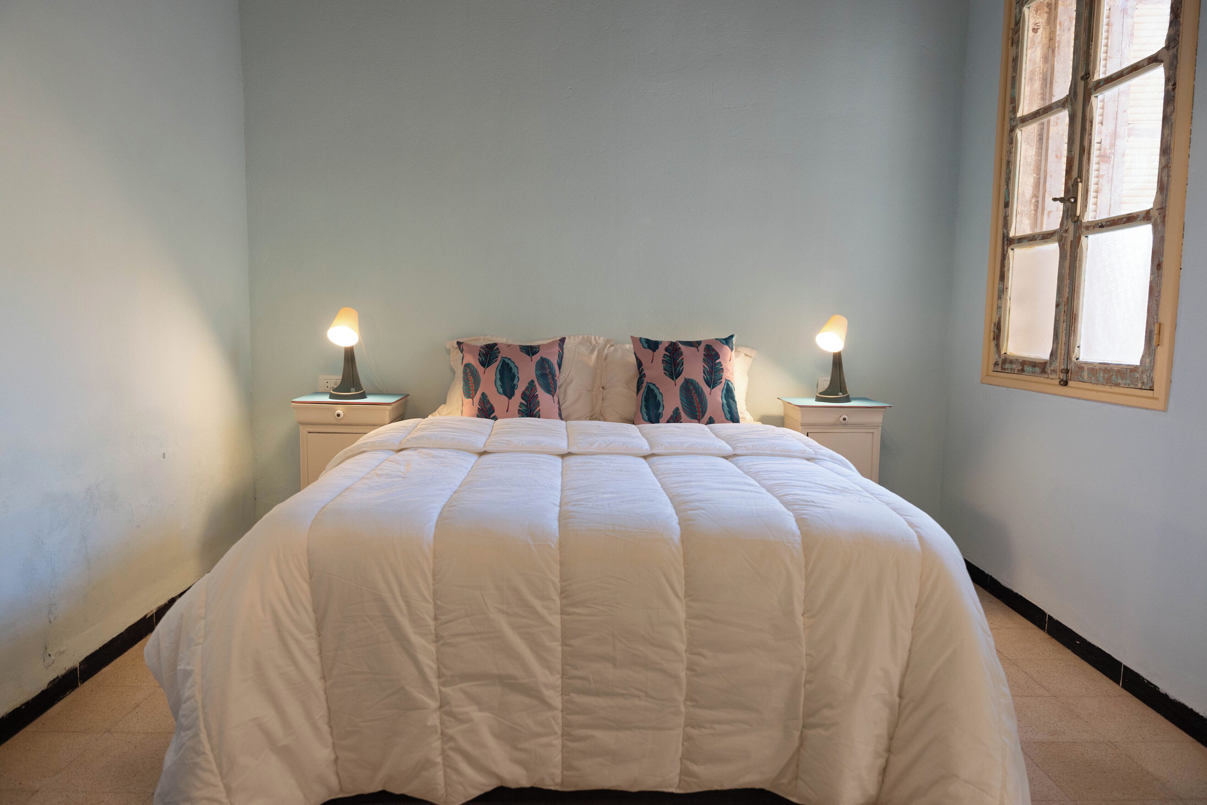 A bedroom with a bed, two bedside tables, and a window.