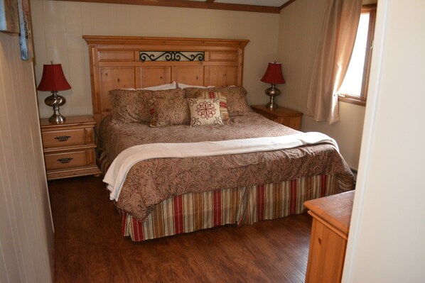 A bedroom with a wooden headboard, a large bed with patterned bedding, two bedside tables with lamps, and a window with curtains. - Spacious Lake Harmony Rental With Hot Tub, Pool Table, Custom Bar And Much More! (Lake Harmony)
