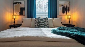 A bedroom with a bed, two bedside tables with lamps, a window with blue curtains, and two wall-mounted paintings. - All king beds, bike garage, Near Back 40 (Bella Vista)