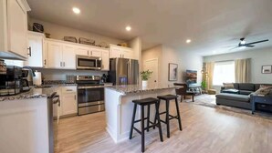 A modern kitchen with stainless steel appliances, a central island with bar stools, and a dining area with a sofa and a coffee table. - All king beds, bike garage, Near Back 40 (Bella Vista)