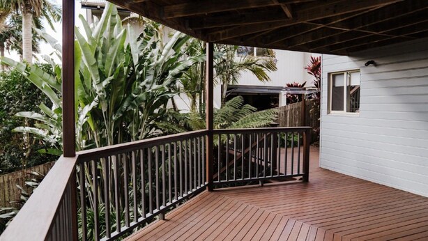 Una terraza de madera con baranda metálica, rodeada de exuberante follaje tropical.