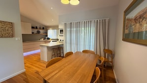 Una cocina moderna con armarios blancos, una isla central y un comedor con mesa y sillas de madera.