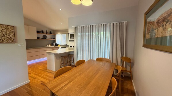 Une cuisine moderne avec des meubles blancs, un îlot central et un coin repas comprenant une table et des chaises en bois.