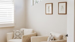Una habitación con dos sillones color beige, uno con un cojín estampado y otro con un cojín liso. Hay dos ilustraciones botánicas enmarcadas en la pared.