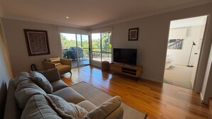 Una sala de estar con sofá, televisión y puertas corredizas de vidrio que dan a un balcón.