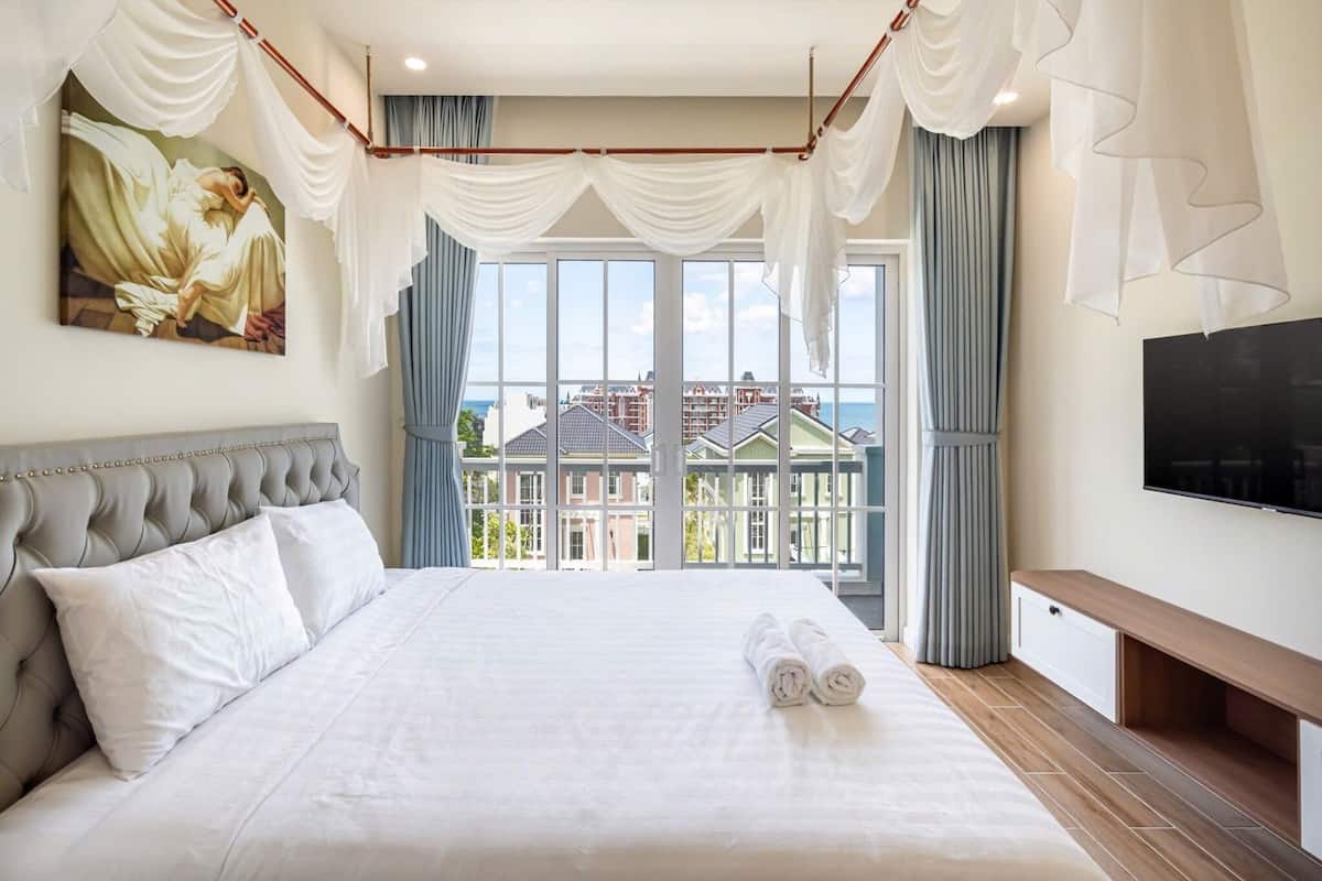 Ein Hotelzimmer mit einem großen Bett, einem Gemälde, einem Fernseher und Blick auf Gebäude sowie ein Gewässer.