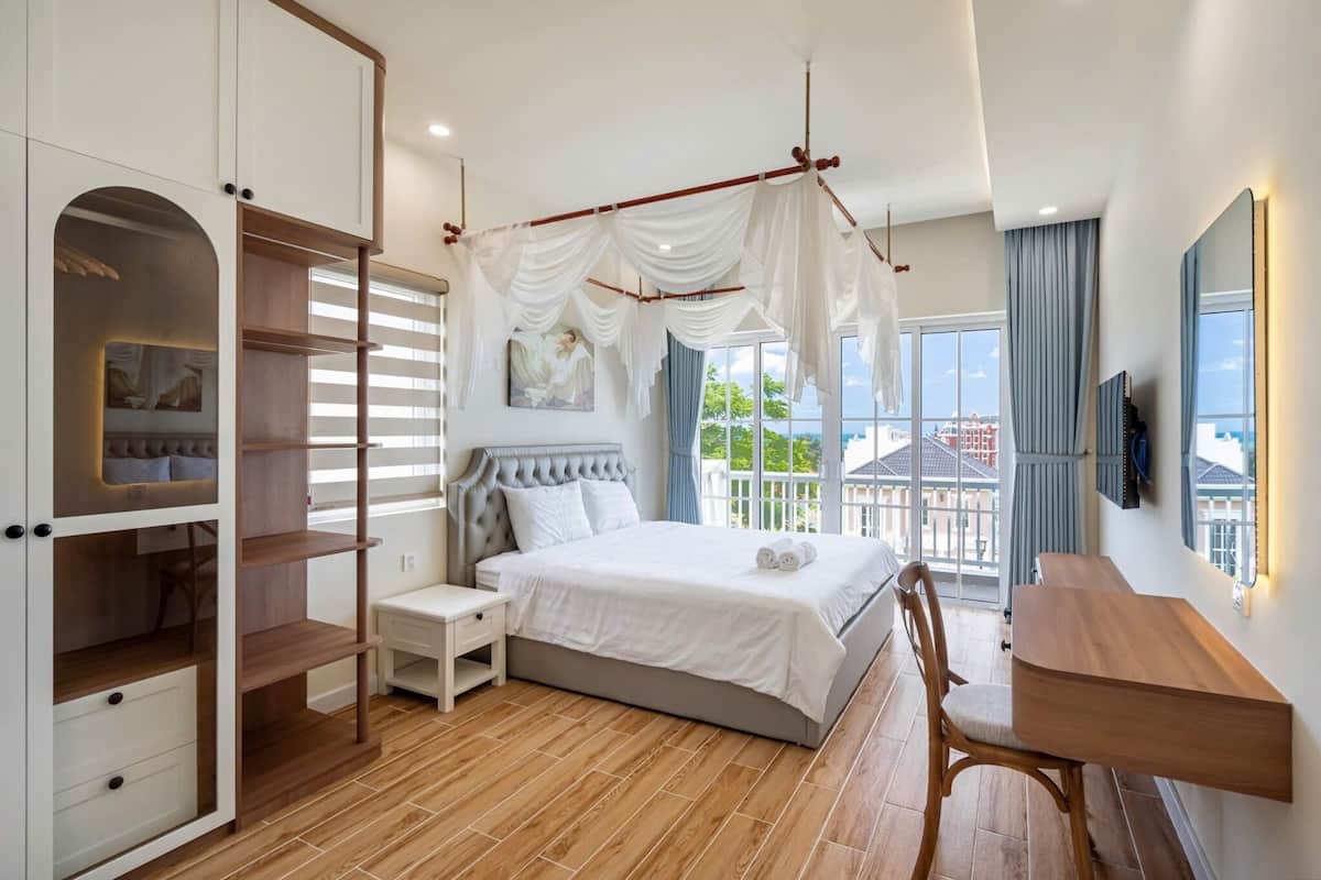 Ein Schlafzimmer mit Bett, Kleiderschrank, Schreibtisch und Blick auf Gebäude.