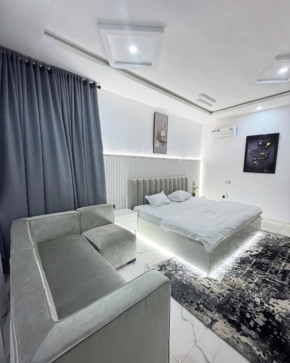 A modern bedroom with a large bed, a sofa, a bedside table, and a patterned rug.