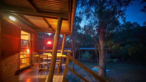 A wooden deck with outdoor seating, a pool, and a view of trees and a building in the background.