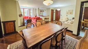 A dining area with a wooden table and chairs, a red sofa, and a kitchen in the background. - Apê Bosque do Silêncio (Campos do Jordão)