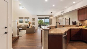 A modern kitchen with a marble countertop, wooden cabinets, and a built-in dishwasher. - Ocean Views and Newly Remodeled!  7G Halii Kai (Waikoloa Beach Resort)