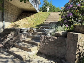 Un escalier en pierre, avec des marches menant à un bâtiment, est entouré de verdure et de vases décoratifs.