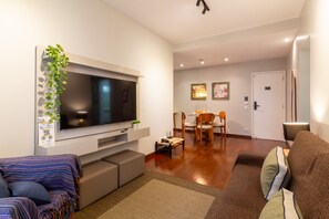 A living room with a flat-screen TV, a sofa, a dining area with chairs, and a door. - Near Rodrigo de Freitas Lagoon | PC308 (Rio de Janeiro)