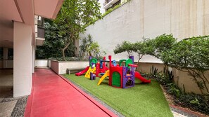 A children's play area with a slide and climbing structures, surrounded by greenery and a red pathway. - Near Rodrigo de Freitas Lagoon | PC308 (Rio de Janeiro)