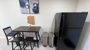 Et kompakt køkken med et sort køleskab, et træ-verdenskort på væggen og et lille bord med stole.