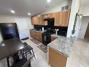 A kitchen with wooden cabinets, a black stove, a microwave, and a dining area with a table and chairs. - Laguna Lounge - Private, Fully Stocked, Central, King bed, Washer/Dryer (Tucson)
