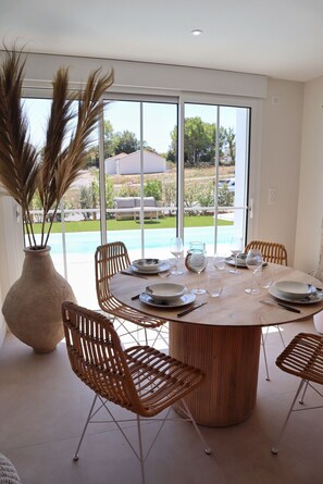 A dining area with a round table, six wicker chairs, and a large vase of dried plants. - Villa 3 – pool – golf – nature – 6 people (Talmont-Saint-Hilaire)