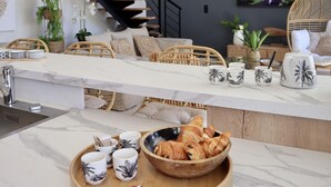 Cozinha moderna com bancada de mármore, bandeja de madeira com doces e um espaço para café.