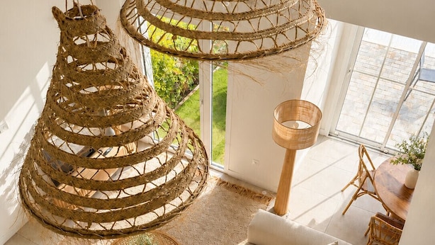 A modern living room with a sofa, woven hanging chairs, a round coffee table, and a view of greenery outside.