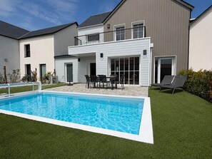 Ein modernes, zweistöckiges Haus mit Swimmingpool, Gartenmöbeln und einem gepflegten Rasen.