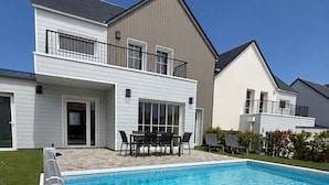 A modern two-story house with a swimming pool, a patio with outdoor furniture, and a well-maintained lawn.