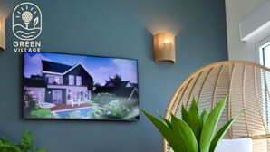 A modern living room with a glass coffee table, a woven chair, and a television displaying a house.