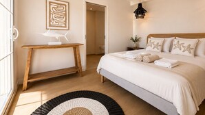 A bedroom with a bed, a desk, a painting, and a hanging light fixture.
