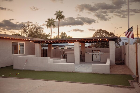 A backyard with a barbecue area, a putting green, and an American flag. - Fun Compound! EV charger, mini-golf, pool, B-ball, Work station, BBQ & Laundry (Tucson)