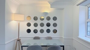 A dining area with a glass table, two upholstered chairs, a floor lamp, and a wall-mounted mirror arrangement. - Flat in Bethnal Green (London)