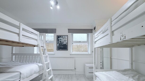 A room with bunk beds, a ladder, a radiator, and a window with a picture on the wall. - Flat in Bethnal Green (London)
