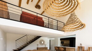Un loft espacioso con techo alto, una escalera, un comedor y una sala de estar con sofá y mesas redondas.