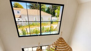 Una sala de estar moderna con un sofá, dos lámparas colgantes de ratán, un televisor y vistas a una zona residencial a través de ventanas amplias.