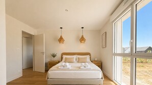 Un dormitorio con una cama grande, dos mesitas de noche, una mesilla auxiliar, una ventana y una puerta.