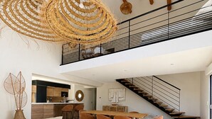 Un interior moderno con sofá, mesa de comedor, sillas, una escalera y una lámpara colgante.