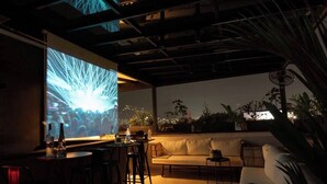 An outdoor seating area with a modern design, featuring a sofa and chairs, a bar area, and a large screen displaying an image. - Poblado 12 Bedroom,  2 Jacuzzis, Rooftop, Staffed (Medellín)