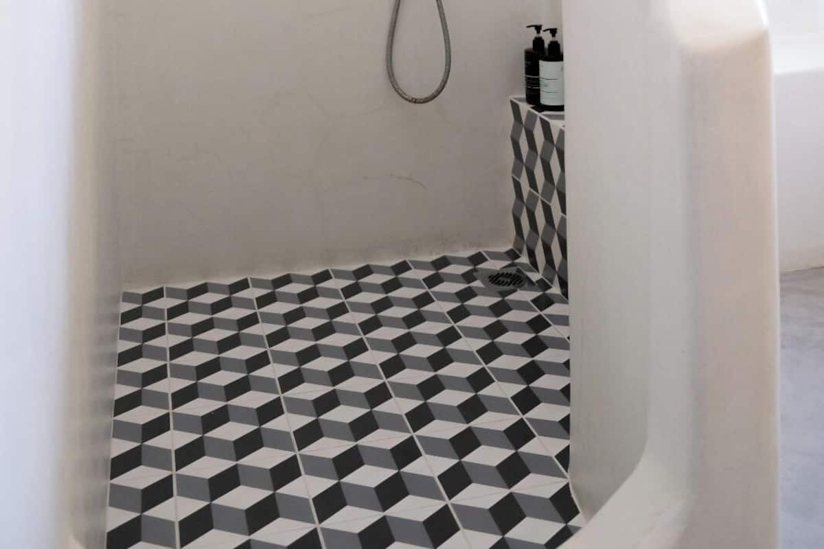 A shower with a geometric floor pattern, a handheld showerhead, and a wall-mounted control.