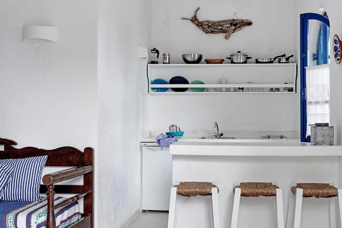 A compact kitchen with white walls, a wooden bed, and a blue-framed window.
