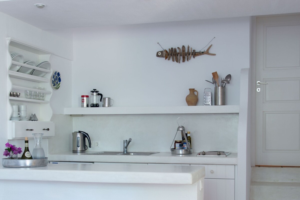 A kitchen with a white island, two bar stools, a coffee maker, and a decorative fish skeleton on the wall.