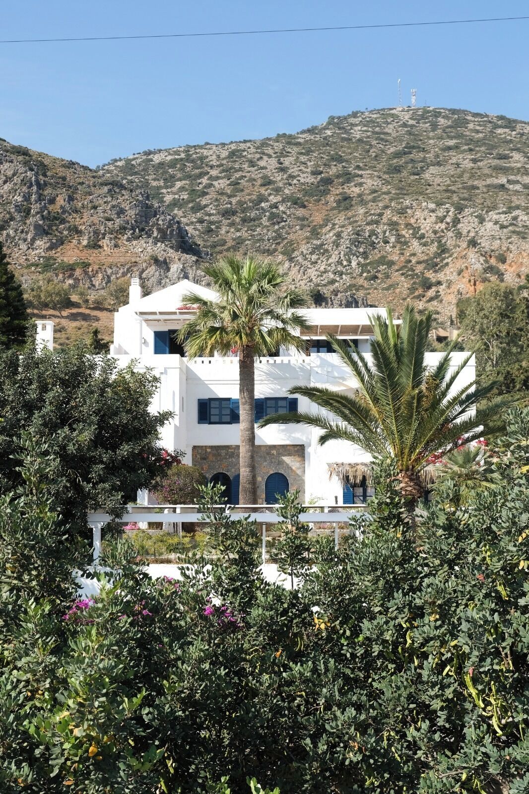 A white building with a stone facade, palm trees, and a mountainous backdrop.