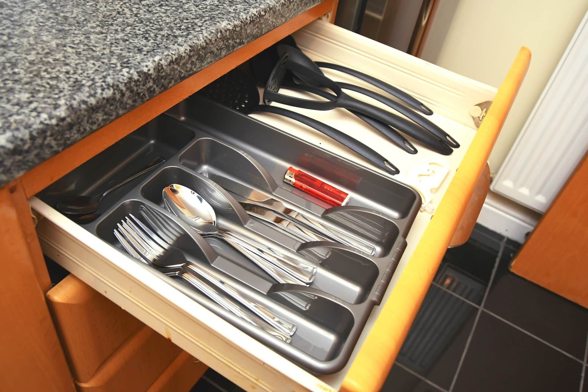 A kitchen drawer with utensils and a red appliance.