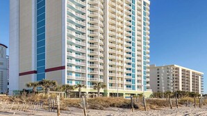 Un grand hôtel doté de nombreux balcons, une plage au premier plan et un ciel dégagé.