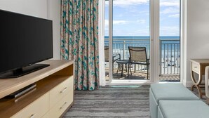 Une chambre d’hôtel équipée d’une télévision, d’un canapé, d’une lampe, d’un balcon avec vue sur l’océan et d’une table avec des chaises.